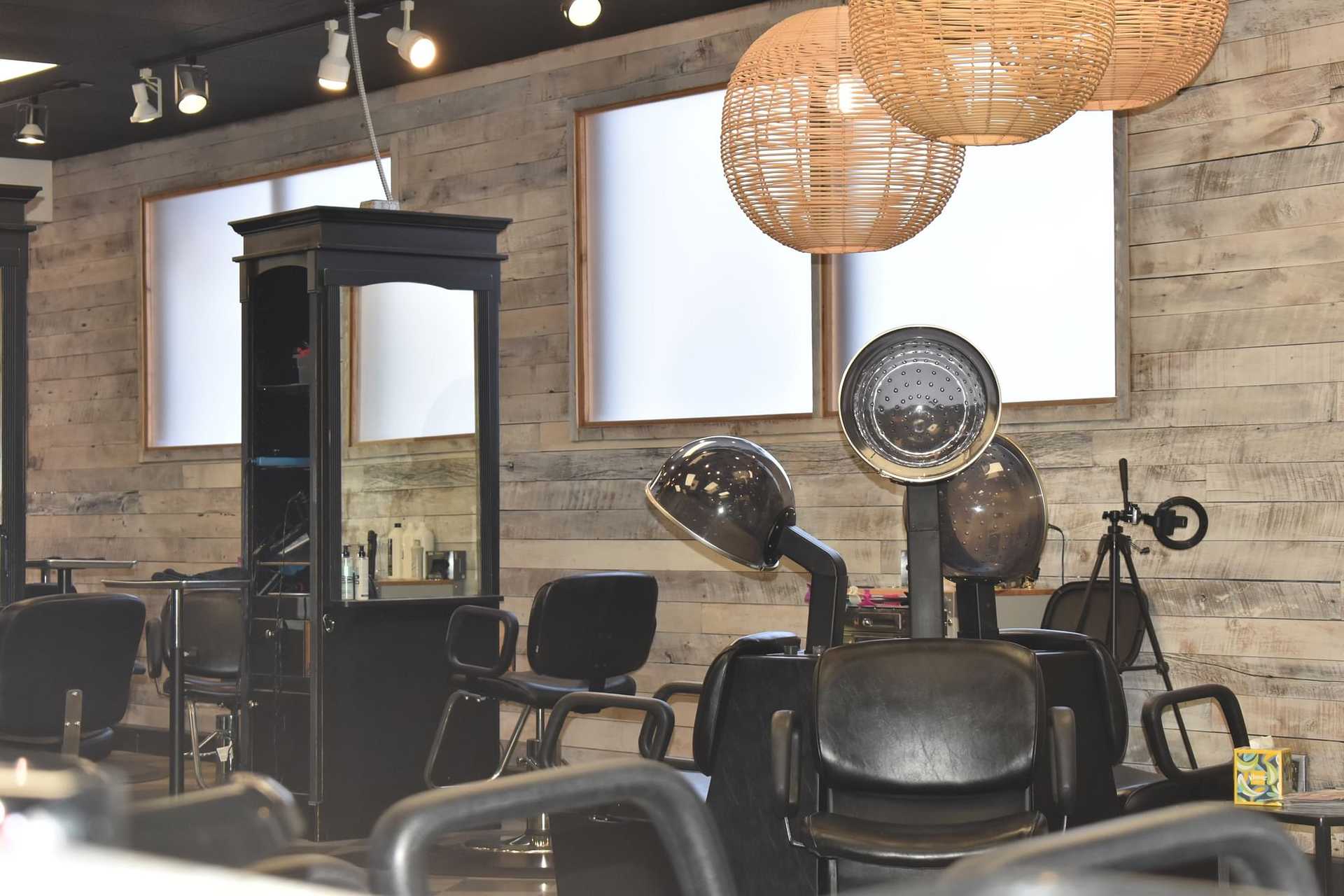 Modern hair salon with styling chairs, hair dryers, and wooden wall decor with large windows.