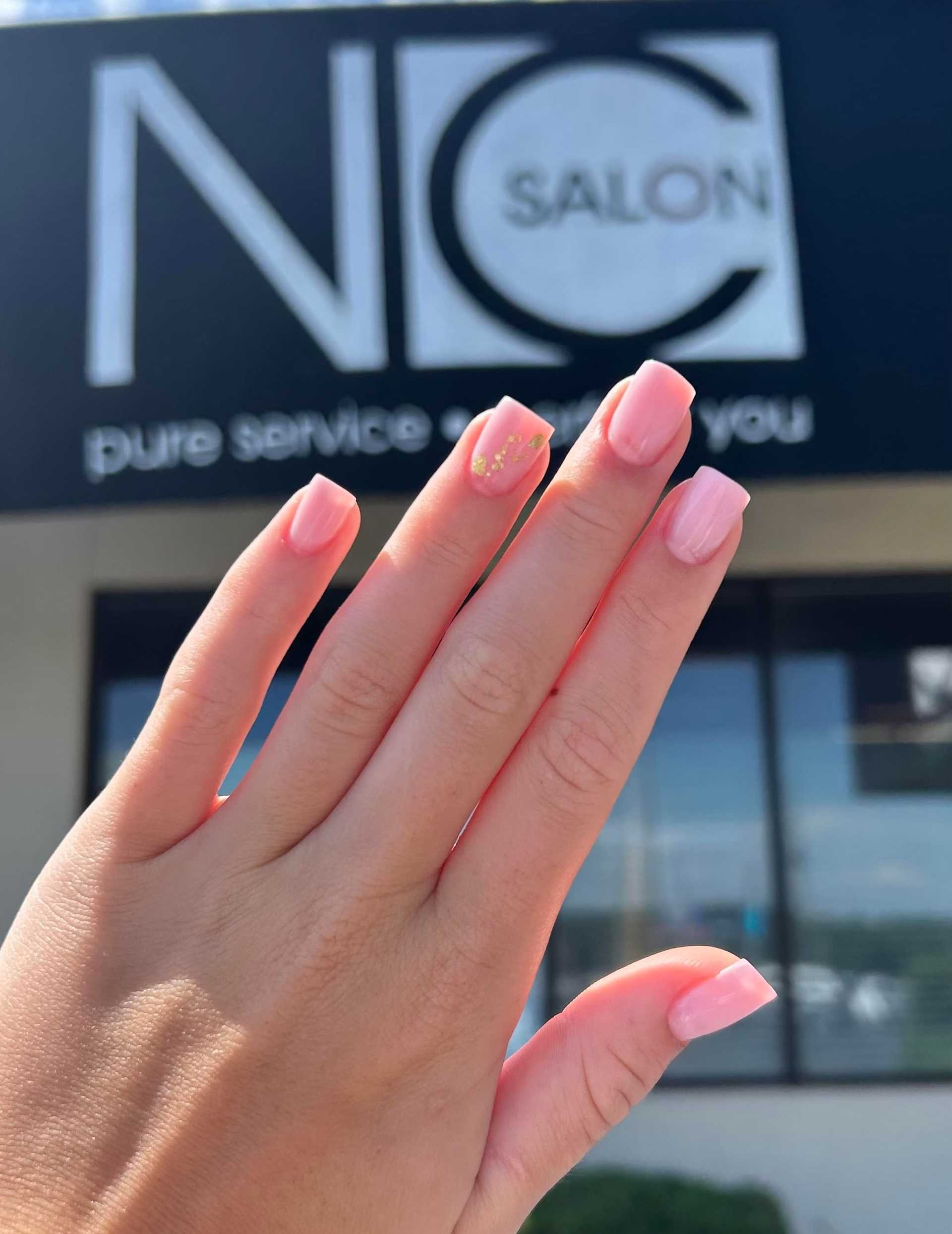 Hand with pink manicured nails in front of NC Salon sign outside a building.