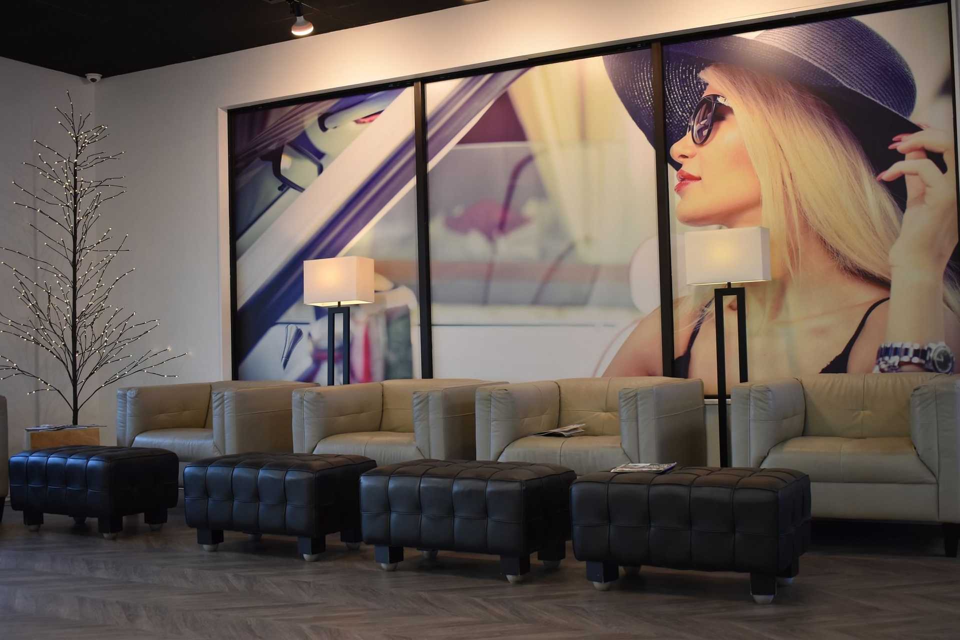 Modern lounge area with beige sofas, black ottomans, floor lamps, and a stylish poster backdrop.